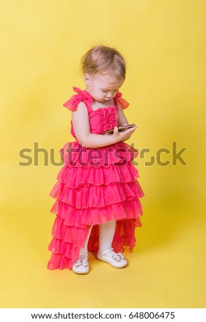 Girl toddler in a pink dress on a yellow background holding a smartphone