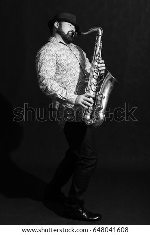 Man in hat with saxophone on dark background, black and white photo