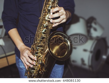 musician plays tenor saxophone on stage with blurred music instrument background