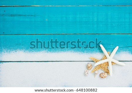 Collection of seashells and starfish in sand border on antique rustic teal blue wood background; blank wooden beach sign with copy space