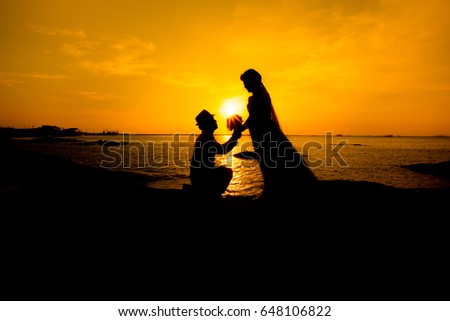 A silhouette of a young man, down on one knee and holding a bouquet, proposing to his girlfriend.will you marry me images.Young couple in love at beautiful sunset.inspired by glistening gold.