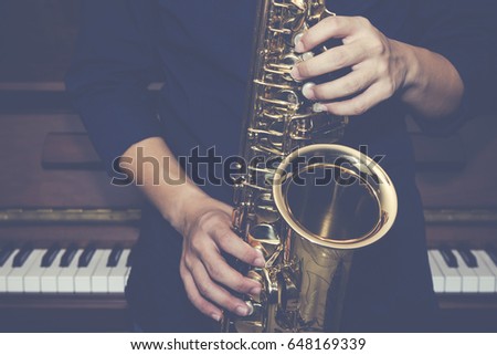 close up of saxophone Player hands  playing alto sax musical instrument over the piano  background,  closeup with copy space, vintage tone,  can be used for music background

