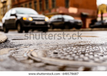 Rainy day in the big city, the headlights of the approaching car on the road. Close up view of a hatch at the level of the asphalt