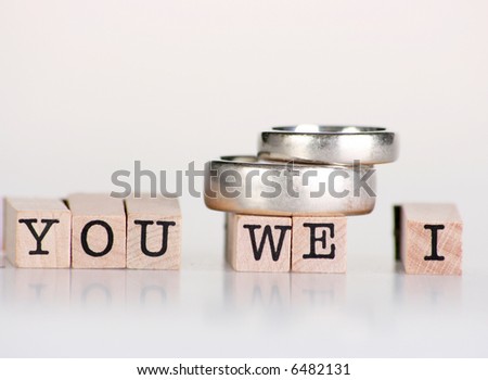 Wedding rings sitting on top of wooden stamps saying “You We I”