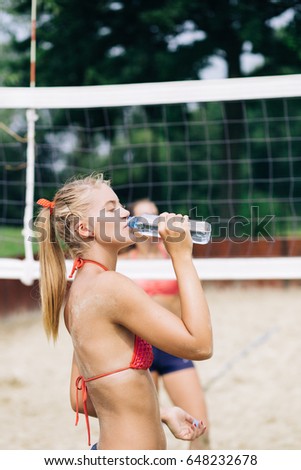 Beautiful young woman drinking water from bottle after playing beach volleyball.