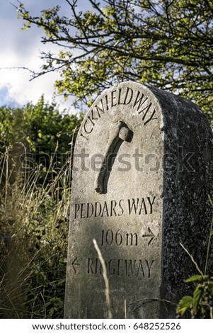 Concrete public footpath marker in the countryside on a sunny day.