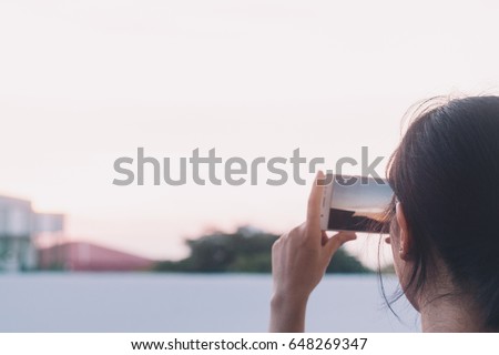 Girl taking photo of sunset with phone camera on rooftop