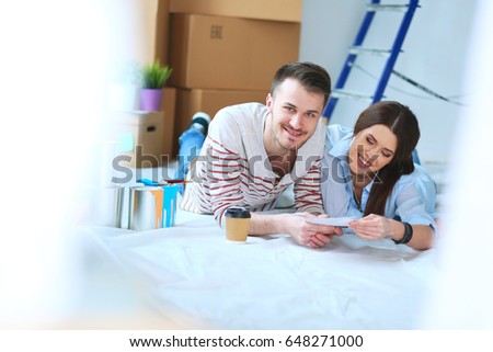 Couple choosing paint color from swatch for new home lying on wooden floor