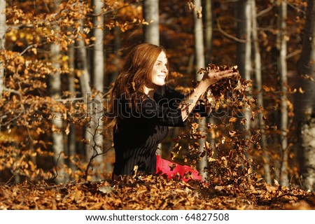 Beautiful young girl sitting through autumn leaves in the middle of the forest, meditating and relaxing