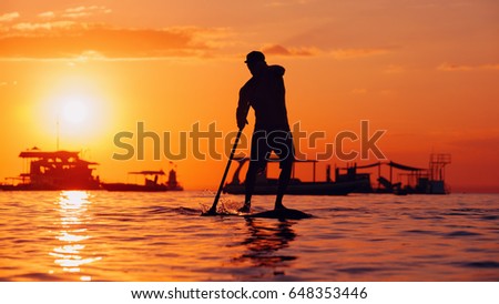 Active paddle boarder. Black sunset silhouette of young sportsman paddling on stand up paddleboard. Healthy lifestyle. Water sport, SUP surfing tour in adventure camp on family summer beach vacation