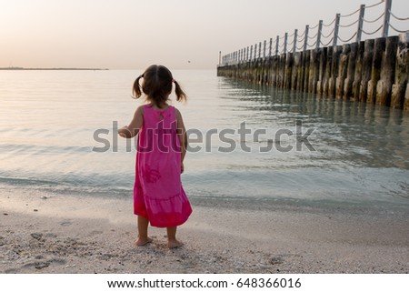 Little girl playing on the beach at sunset time