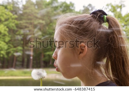 Beautiful child blowing away dandelion flower in spring toned