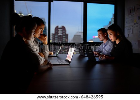 business team working with computer overtime at night and low light, teamwork businessman and businesswoman