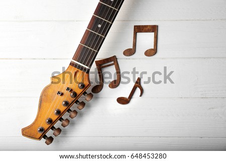 Musical notes and guitar neck on white wooden background