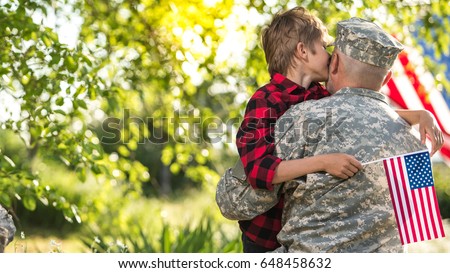 American soldier reunited with son on a sunny day with american flag on the background. wide screen image