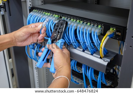 hand of system administrator with network cable connected to patch panel of network gigabit switch and crimping pliers tool Royalty-Free Stock Photo #648476824