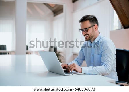 Portrait of young man sitting at his desk in the office Royalty-Free Stock Photo #648506098