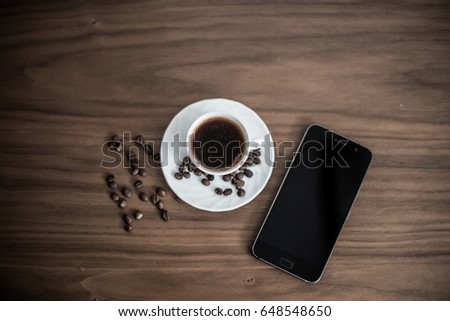 Saved coffee in a cup with a wooden background, green coffee around cups, coffee bean on wooden texture, cell phone next to cups, businessman resting with coffee