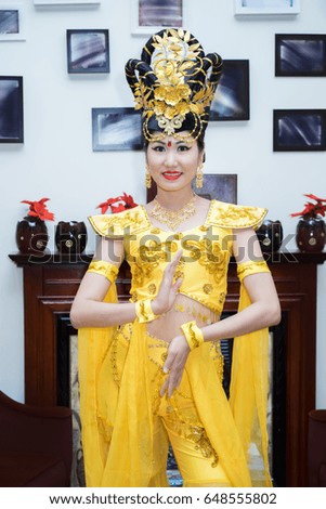 beautiful asian girl in a traditional yellow chinese stage costume standing near the wall with pictures and fireplace