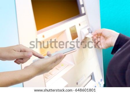 Man use mobile phone, blur image of girl insert the card in to ATM machine as background.