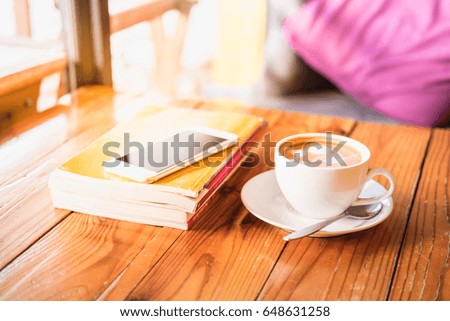 Cup of hot coffee latte with spoon, smart phone and book on wooden table in the coffee shop