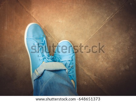 A man in jeans and blue sneakers is standing on the old floor of tiles. Top view. Close-up. Conceptual image young lifestyle.