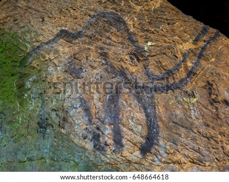 Prehistoric art of mammoth in sandstone cave. Spotlight shines on historical painting. Black carbon mammoth on sandstone wall. Paint of human hunting,  prehistoric picture. Discovery of human history