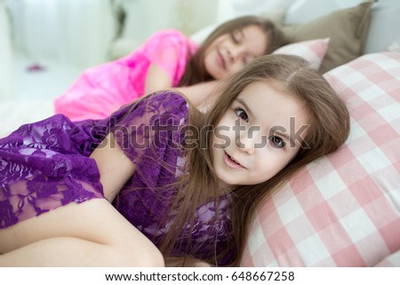 Pretty little girls in pink and purple princess  dresses in white bed with cushions