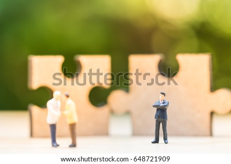 Miniature people: Two confident business man shaking hands during a meeting in front of wooden jigsaw puzzle icon, success, dealing, greeting and partner concept.
