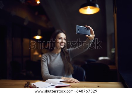 Selective focus on woman's hands with smartphone making selfie on camera for updating profile photo in social networks while spending free time in cozy coffee shop sitting on promotional background