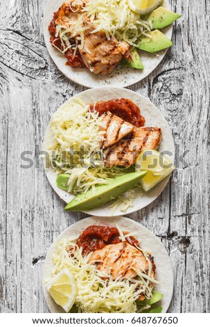 Grilled chicken, avocado, cheese and spicy tomato sauce tortillas on wooden rustic background, top view