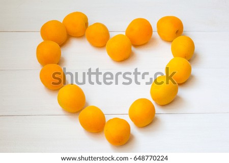 Heart shape of fresh juicy apricots at white wooden background
