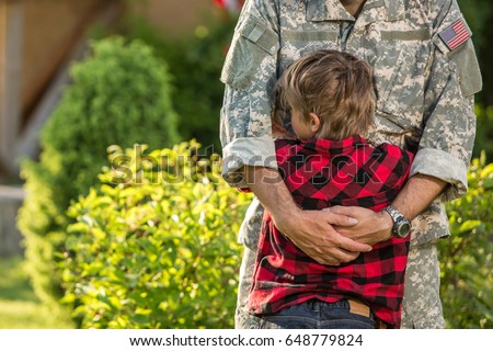 American soldier reunited with son on a sunny day. Cute boy hugs his father concept