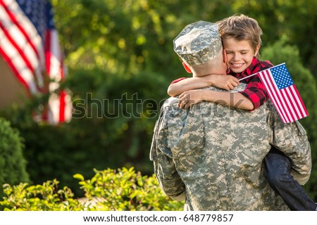 American soldier reunited with son on a sunny day with american flag on the background