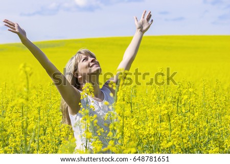 Woman with long hair standing on yellow rapeseed meadow with raised hands. Concept of freedom and happiness