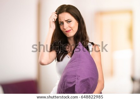 Beautiful young girl with a pillow having doubts in her apartment