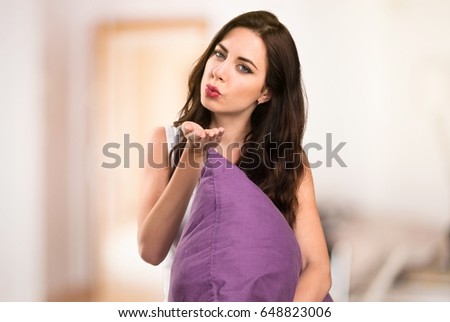 Beautiful young girl with a pillow sending a kiss in her apartment