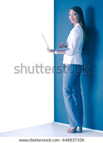Young woman holding a laptop, standing on gray background