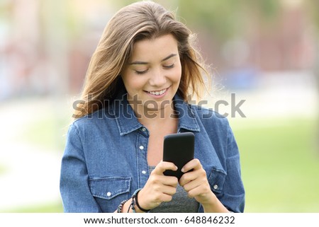 Portrait of a happy teen walking and reading text in a smart phone in the street