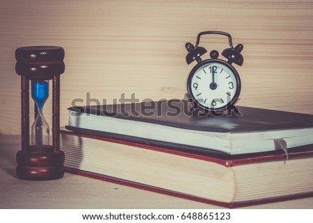 Clock Hourglass Alarm with book on wooden desk