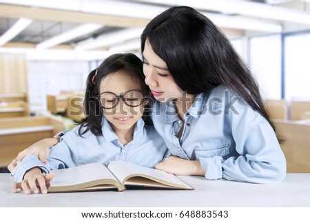 Picture of pretty female teacher teaching her student to read a book while sitting in the classroom