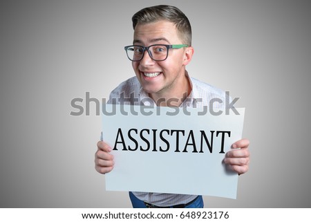 Funny laughing guy (men, student, businessman) of european appearance in casual clothes and glasses is holding a white sheet with text Assistant