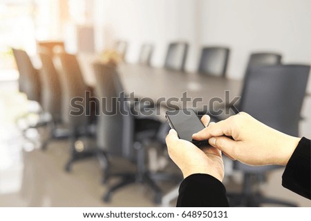 Man using mobile over blurred empty business meeting room 