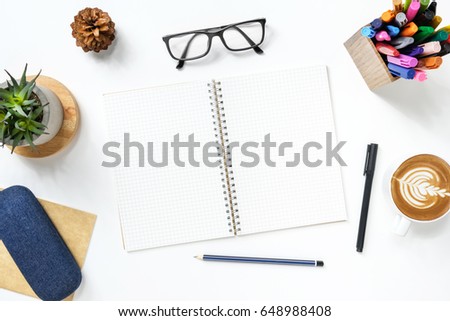 Blank notebook with grid lines is on top of white office desk table with supplies. Top view, flat lay.