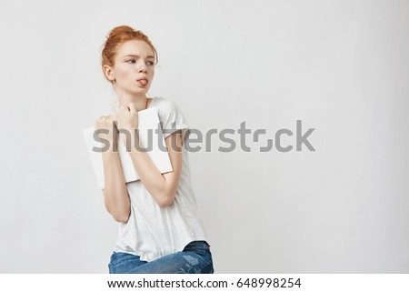 Scared beautiful redhead girl holding book showing tongue.
