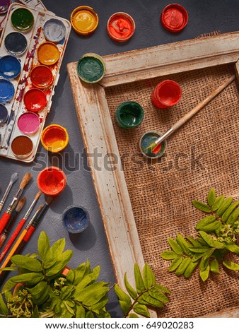 Brushes, acrylic and watercolor paints, a picture in a frame and a canvas, tools for the artist's creativity on a dark background in a vintage style