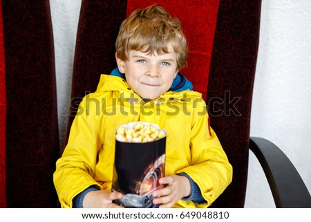 cute blond little kid boy eating popcorn at the cinema before the movie starts. Happy child having fun and waiting for the cartoon or film. Family day, leisure with children