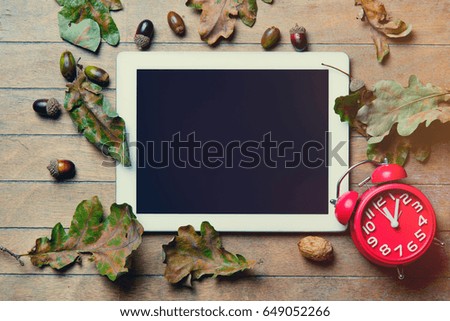 photo of alarm clock and blackboard on wooden table full of foliage, acorns and nuts
