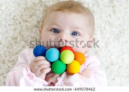 Cute adorable newborn baby playing with colorful wooden rattle toy ball on white background. New born child, little girl looking ath the camera. Family, new life, childhood, beginning concept