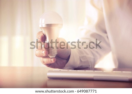 Man's hand holding a light bulb above the keyboard. Concept for business idea and solutions, brainstorming, startup, innovation,  creative work, consulting, research and development.